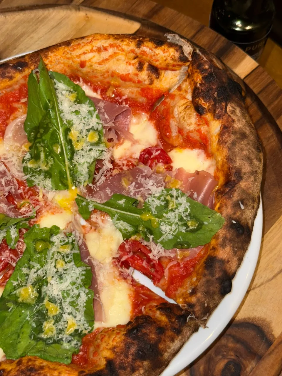 Detalhe de uma pizza da Vila109 com folhas verdes e queijo ralado